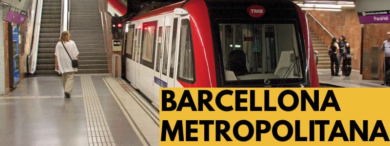 Fotografia di una stazione della metropolitana di Barcellona con il treno in arrivo ed una persona che sta uscendo dalla stazione ed altre che parlano con rettangolo in basso a destra arancione e scritta nera Barcellona Metropolitana