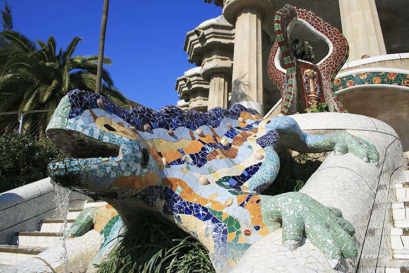 Scultura di una lucertola ricoperta da mosaici colorati tra due scalinate di Parc Güell