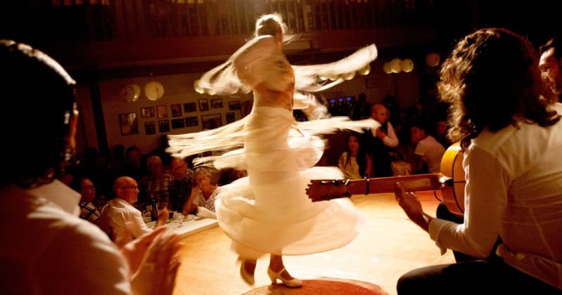 Fotografia di una ballerina di Flamenco vestita di bianco e di un musicista con chitarra sulla destra e pubblico in un locale