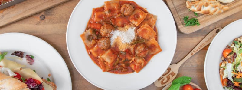 Fotografia dall'alto piatto pasta con sugo ed altri piatti su tavolo di legno