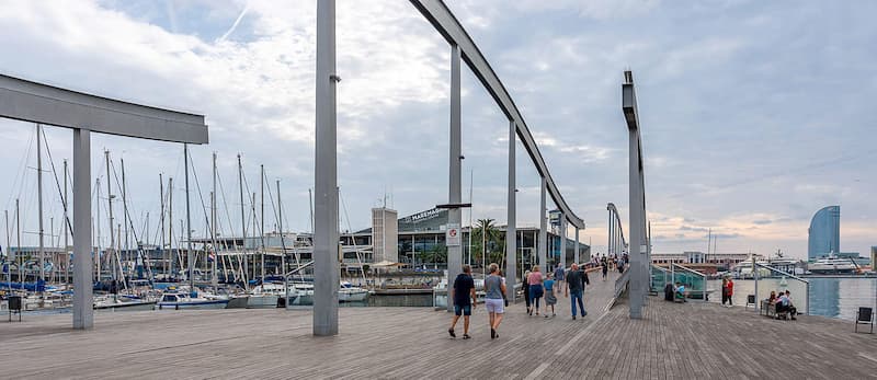 Fotografia Rambla de Mar con pavimento in legno e pali in cemento che decorano il percorso in una giornata nuvolosa con alcune persone che camminano