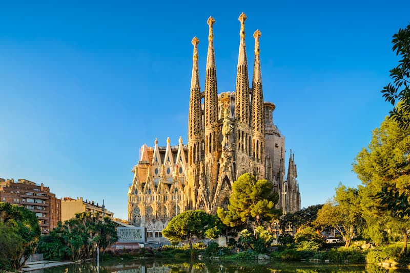 Fotografia esterno Sagrada Familia cielo azzurro ed alberi attorno